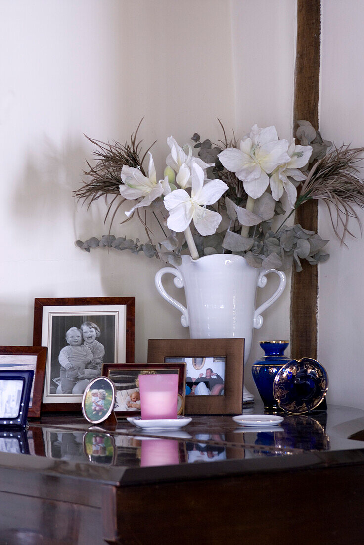 Detail einer weißen Vase mit Kunstblumenarrangement und Familienfotos auf einem Klavier
