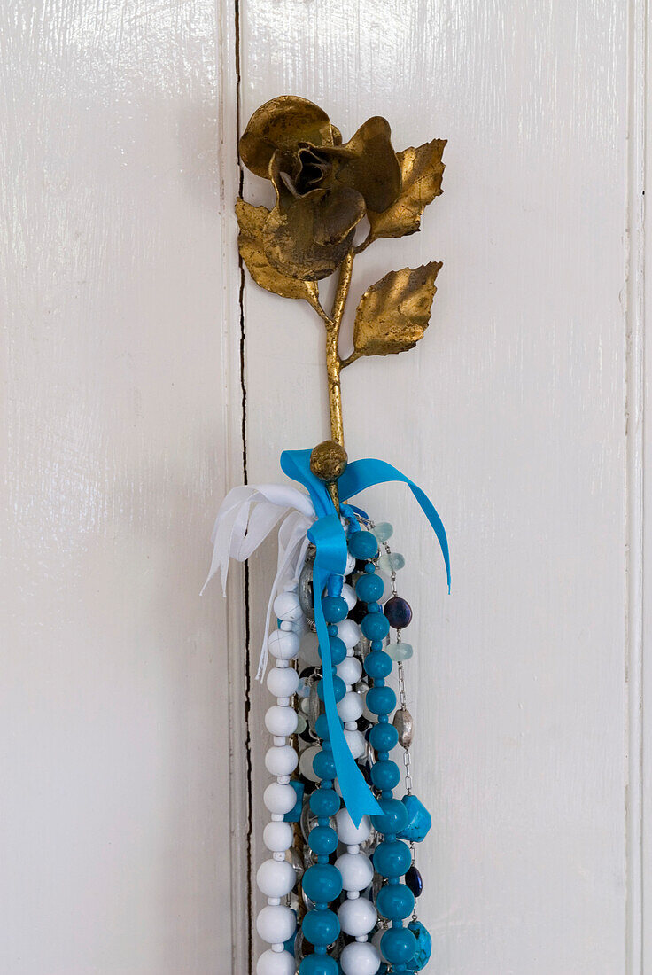 Detail eines Türhakens aus vergoldeter Rose mit bunten Perlenketten und Bändern