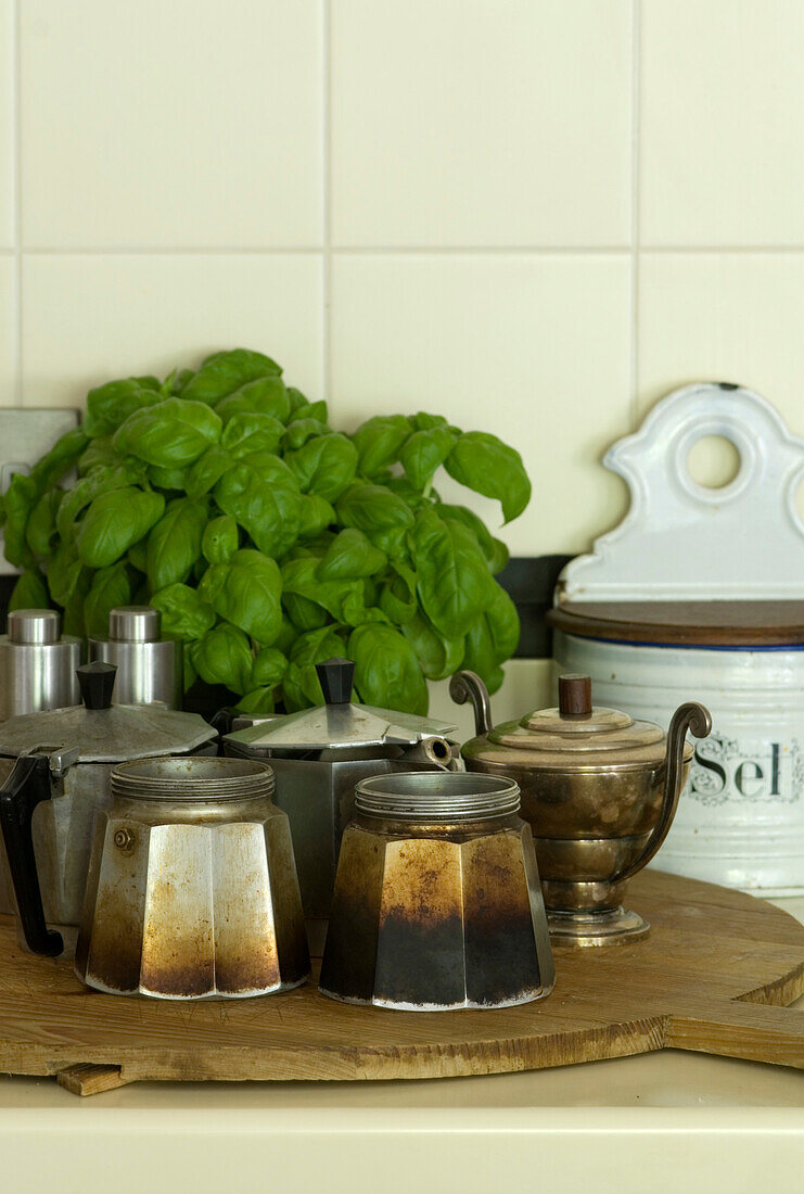 Coffee pots and basil on chopping board in tiled kitchen