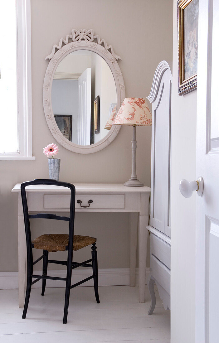 Oval shaped mirror above dressing table with toile du j'ouy lamp and wooden chair