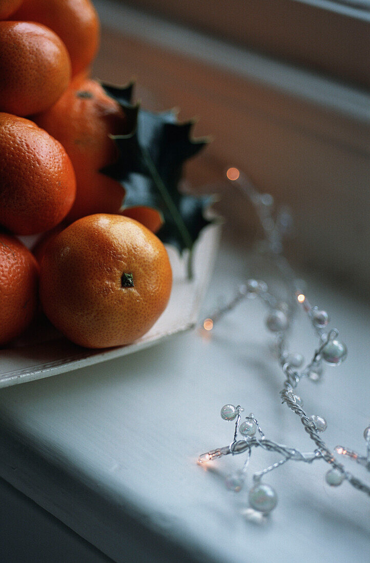 Weihnachtsdekoration mit einem Stapel Orangen und Stechpalmenblättern