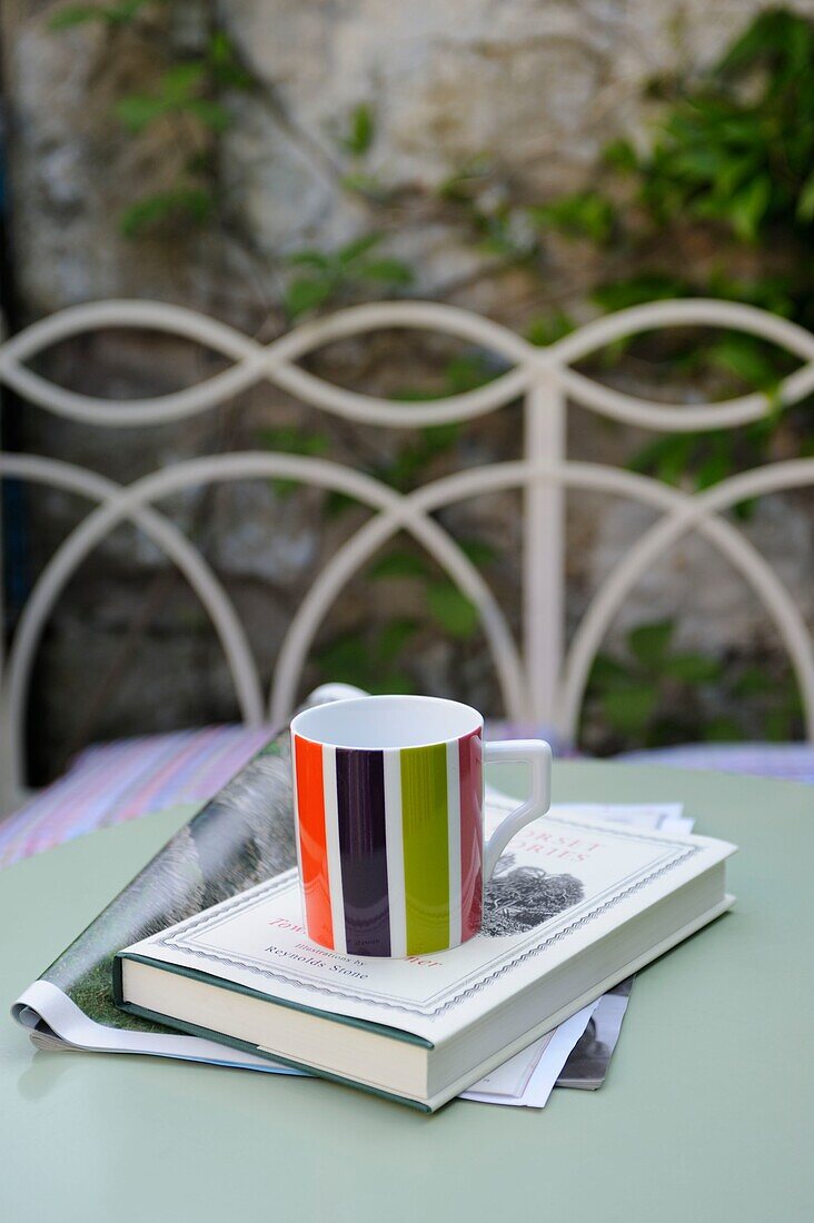 Tasse mit Zeitung und Buch auf einem Tisch im Freien