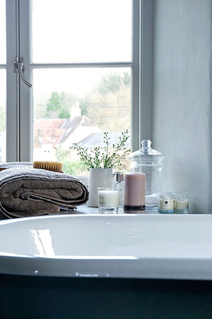 Scented candles and folded towel on windowsill beside bathtub