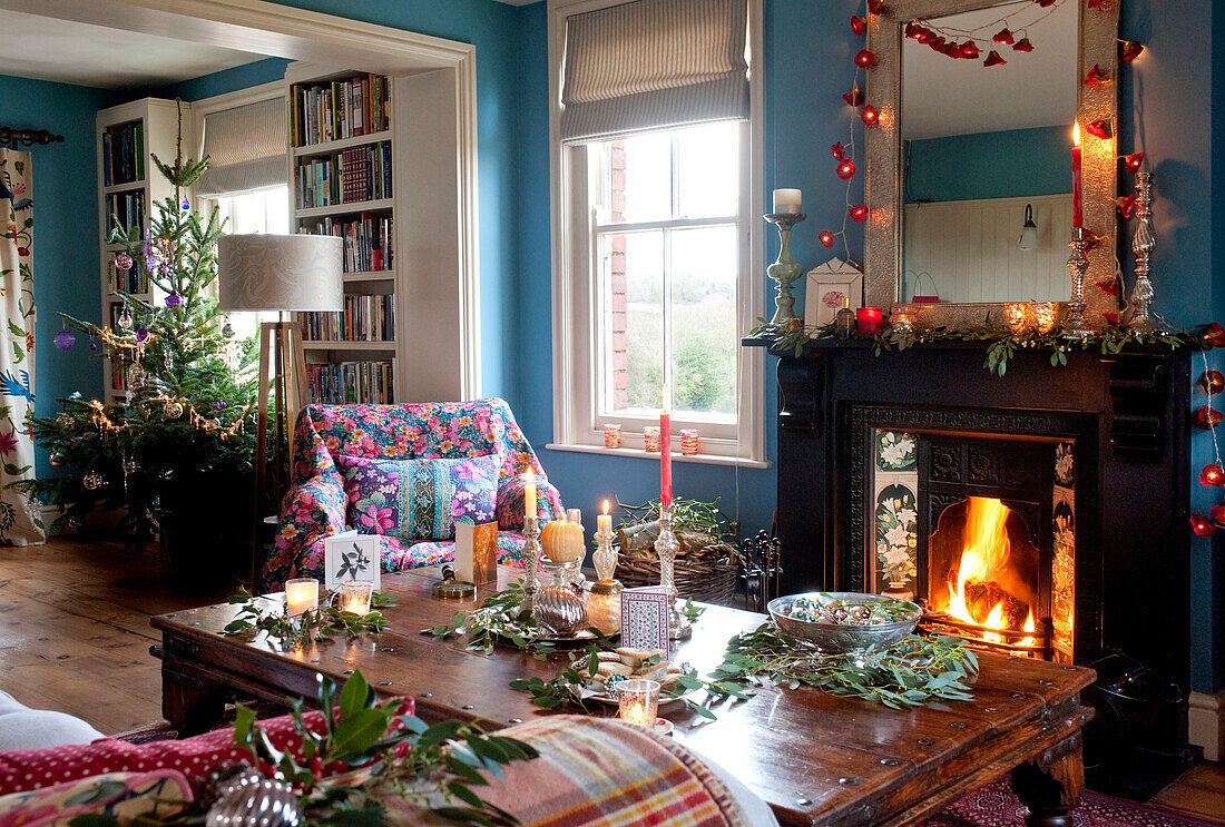 Beleuchtetes Feuer und Lichterketten mit hölzernem Couchtisch in einem Landhaus zu Weihnachten