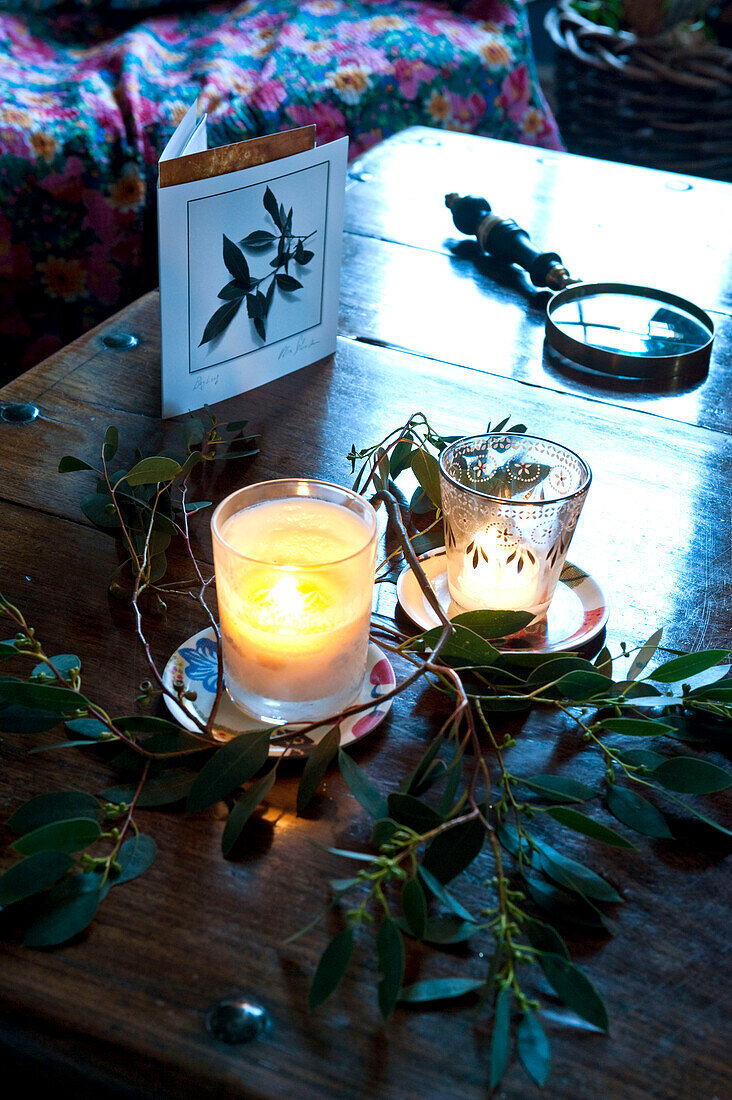 Lit candles and greetings card with magnifying glass and greenery on coffee table at Christmas