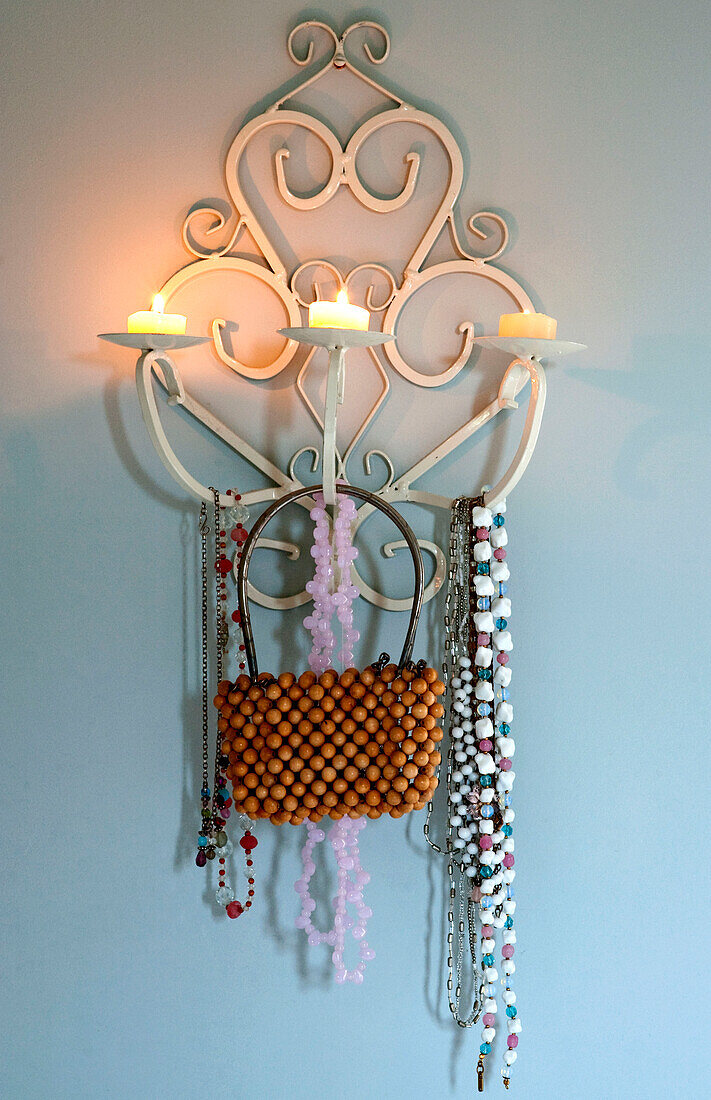 Perlentasche und Halsketten hängen an einem an der Wand befestigten Kerzenhalter