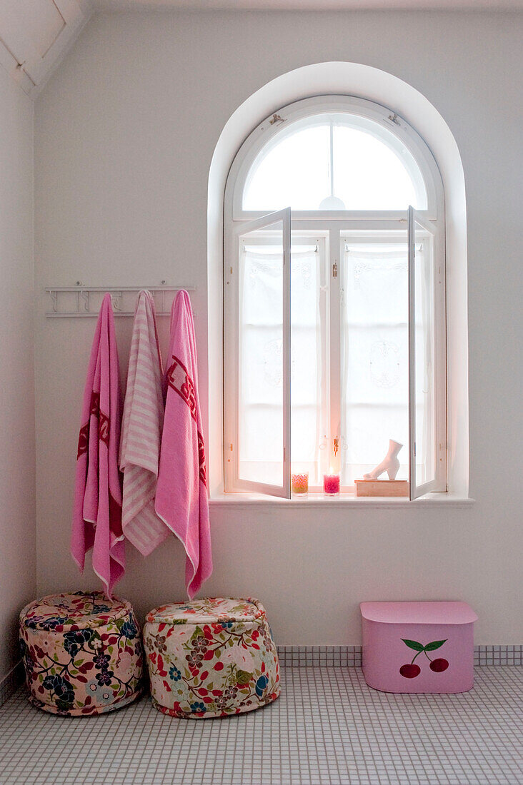 Pink towels above floral pouf at arched window of Odense bathroom
