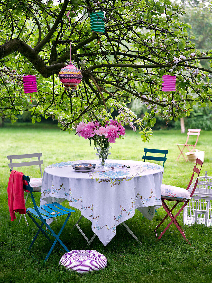 Sommerlicher Gartentisch unter einem Baum mit Papierlaternen, die in einem Baum hängen