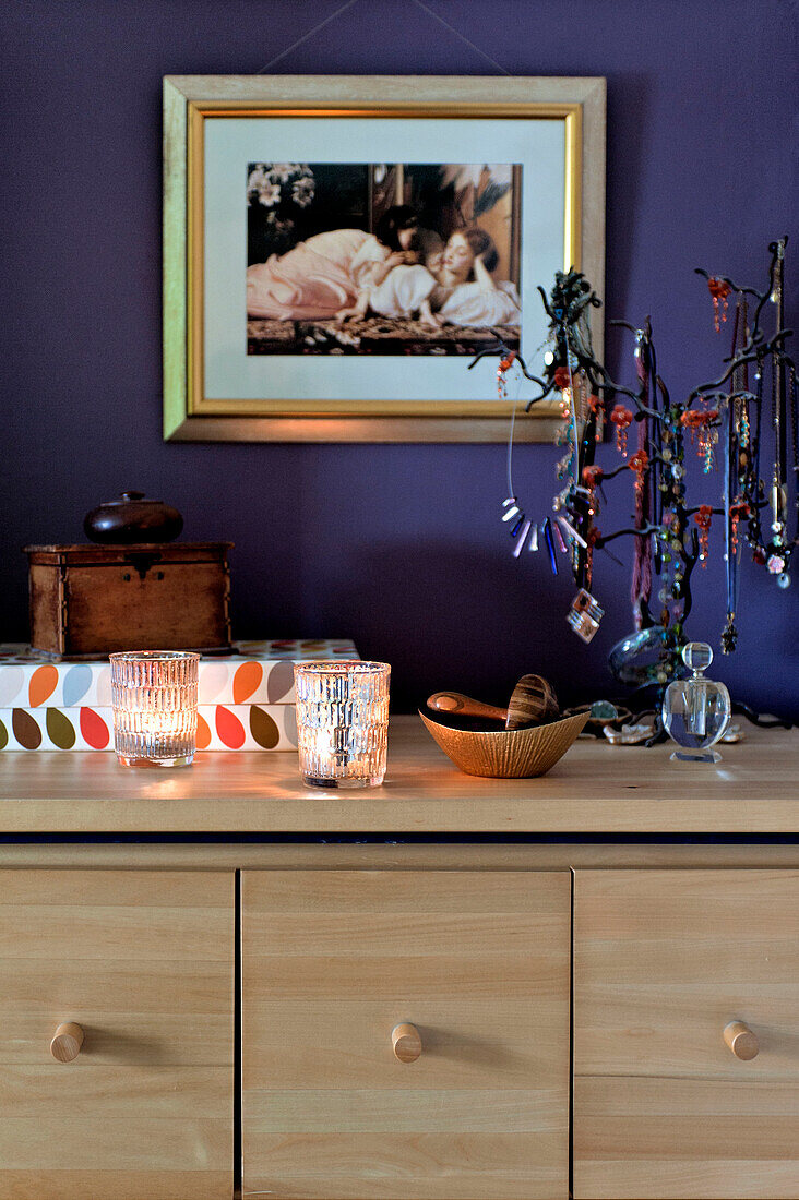 Beleuchtete Kerzen und Schmuckständer auf der Anrichte im lilafarbenen Schlafzimmer eines Hauses in London (UK)