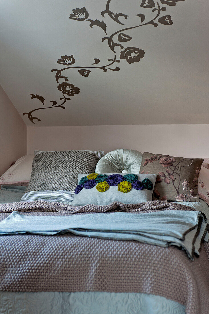 Verschiedene Kissen auf einem Doppelbett unter der Decke mit floraler Wanddekoration in einem Haus in London UK