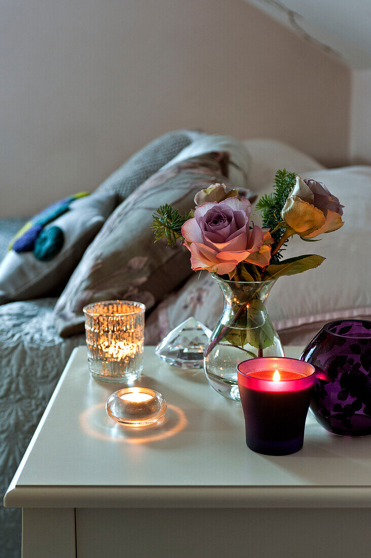 Beleuchtete Kerzen auf einem Nachttisch mit Schnittblumen in einem Londoner Haus im Vereinigten Königreich