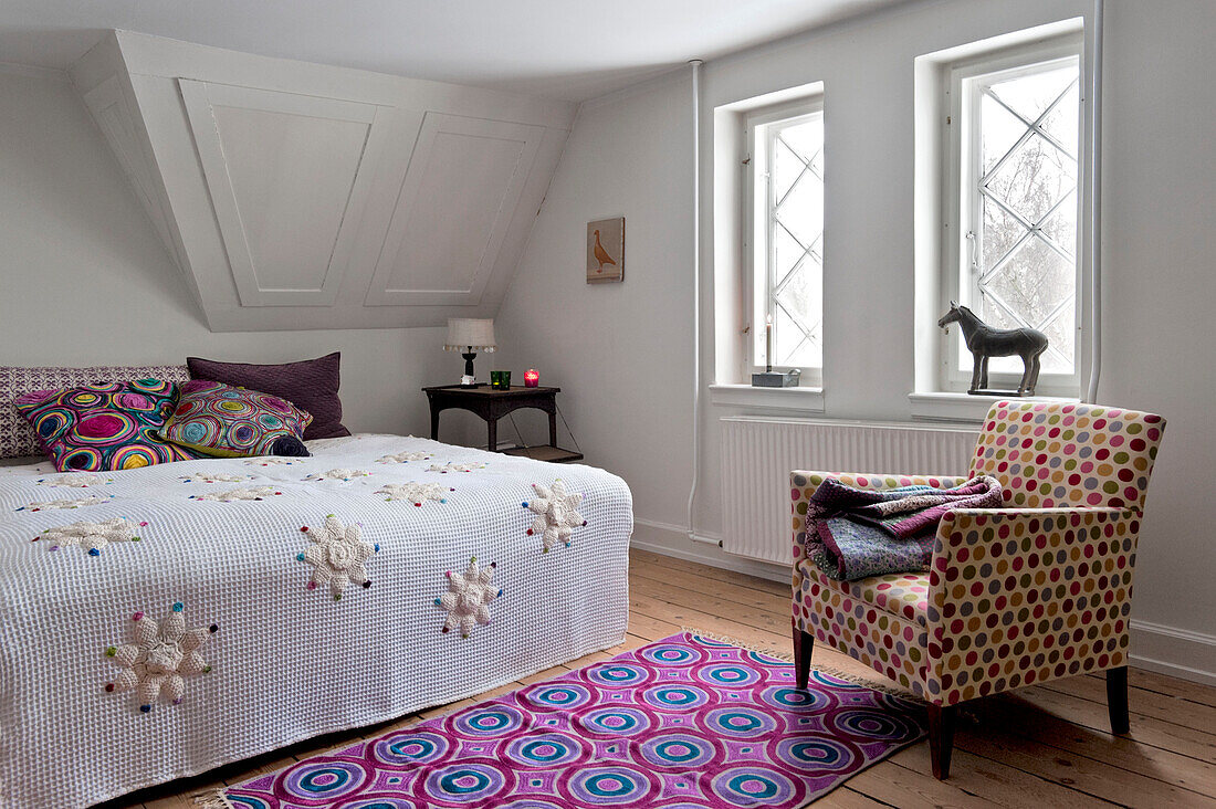 Gefaltete Steppdecke auf einem gepolsterten Stuhl mit bunt gemustertem Teppich in einem modernen Schlafzimmer in Odense Dänemark