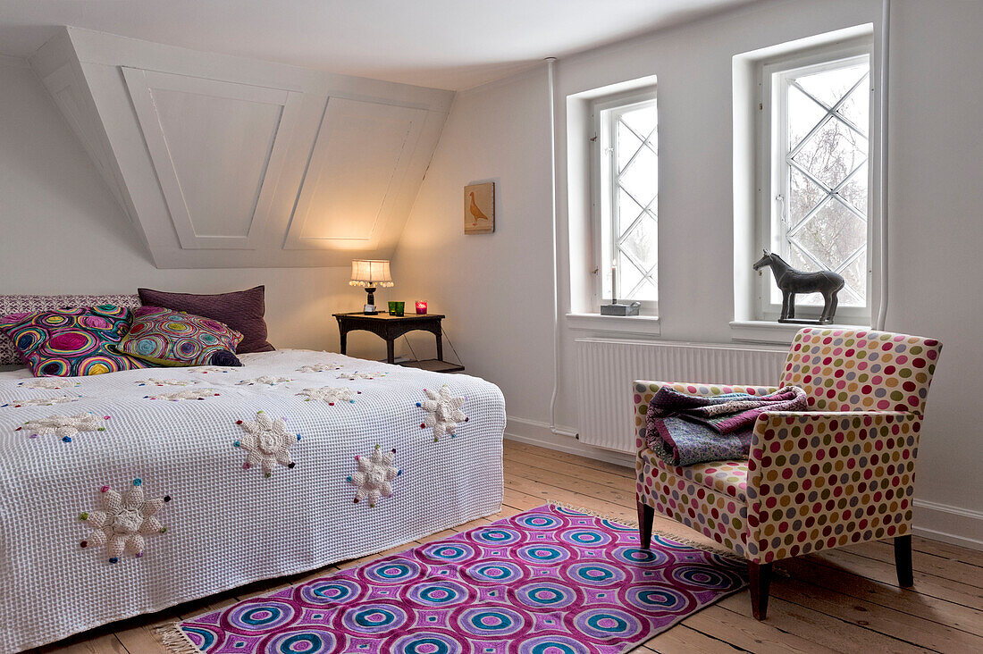 Folded blanket on upholstered chair with brightly patterned rug in modern Odense bedroom Denmark