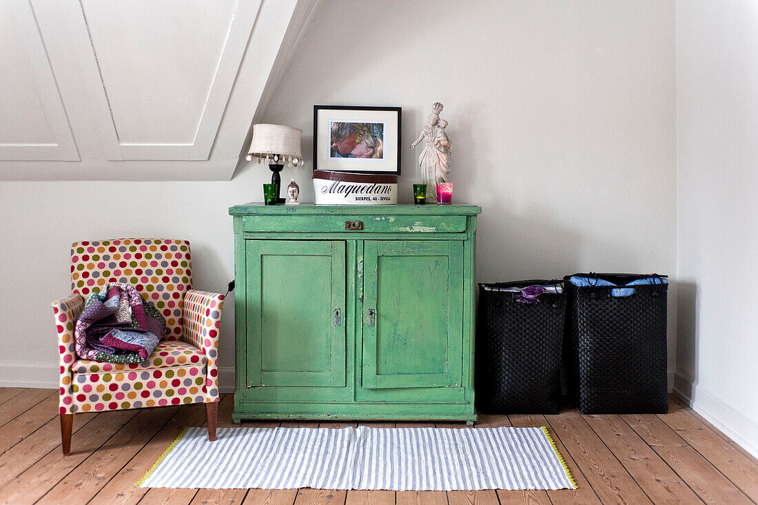 Patterned armchair and green painted cupboard unit with black laundry baskets in modern Odense bedroom Denmark
