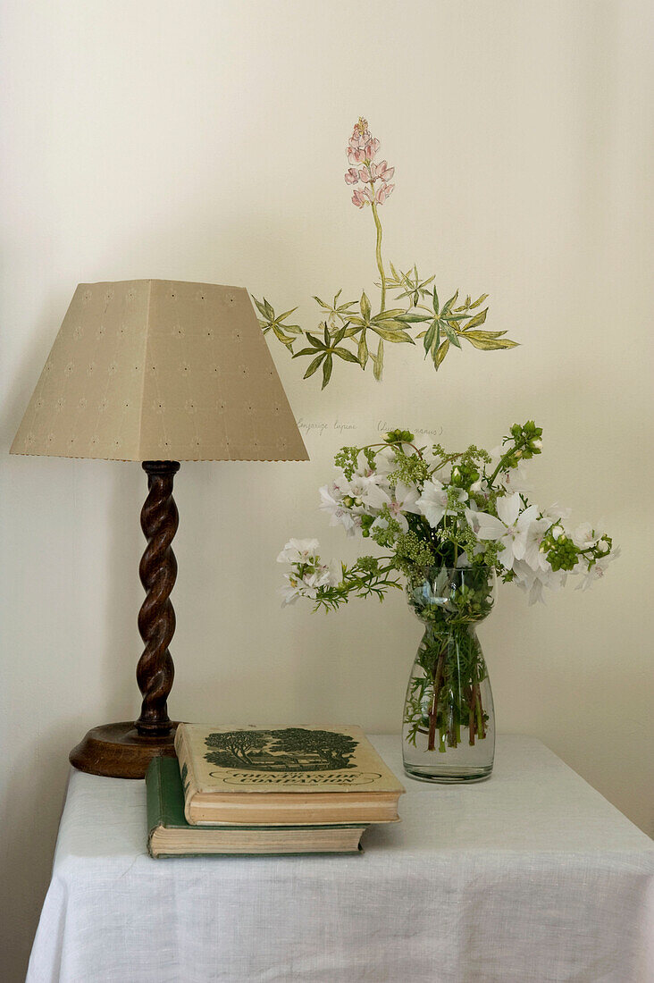 Table lamp and cut flowers below artwork in Devon home