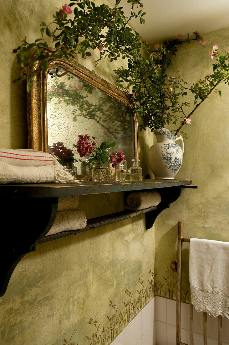 Schnittblumen auf Wandregal mit gerettetem Spiegel und Kletterrosenzweig
