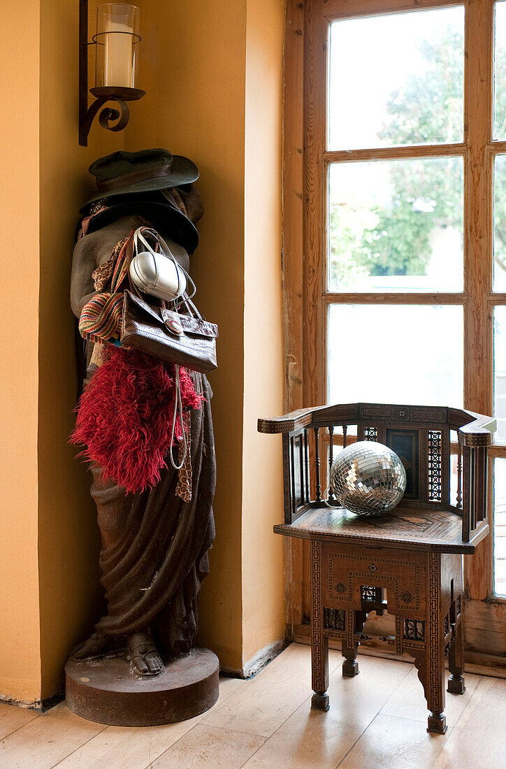 Hats and bags on female statue with antique chair and disco ball in doorway of UK home