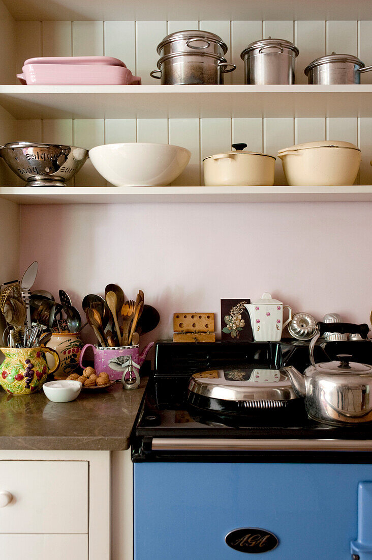 Kitchenware and utensils on open shelving with kettle on oven in London home UK