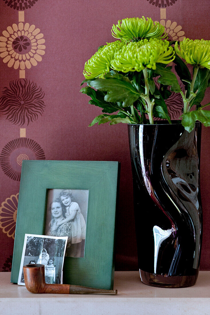 Vase mit grünen Chrysanthemenblüten und schwarz-weißen Familienfotos auf dem Kaminsims in einem Londoner Haus UK