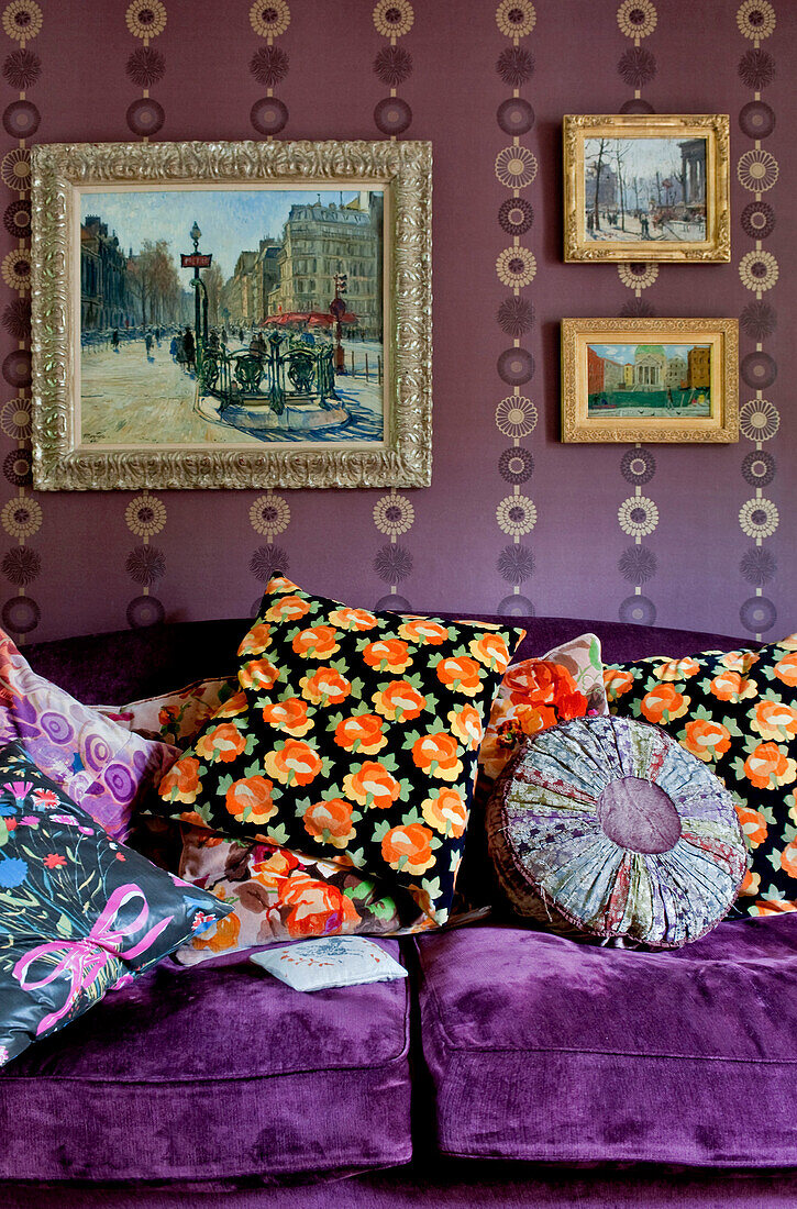 Assorted and brightly coloured cushions on purple sofa under artwork in London home UK