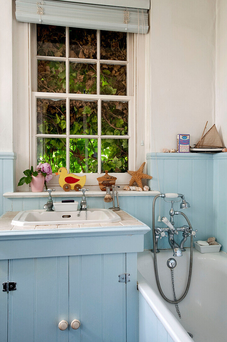 Waschbecken und Duscharmatur am Fenster eines hellblau gestrichenen Badezimmers in einem Londoner Haus UK