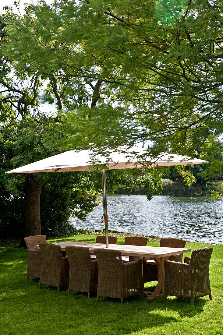 Tisch und Stühle mit Sonnenschirm unter einem Baum am Seeufer im Garten eines Hauses in West London England UK