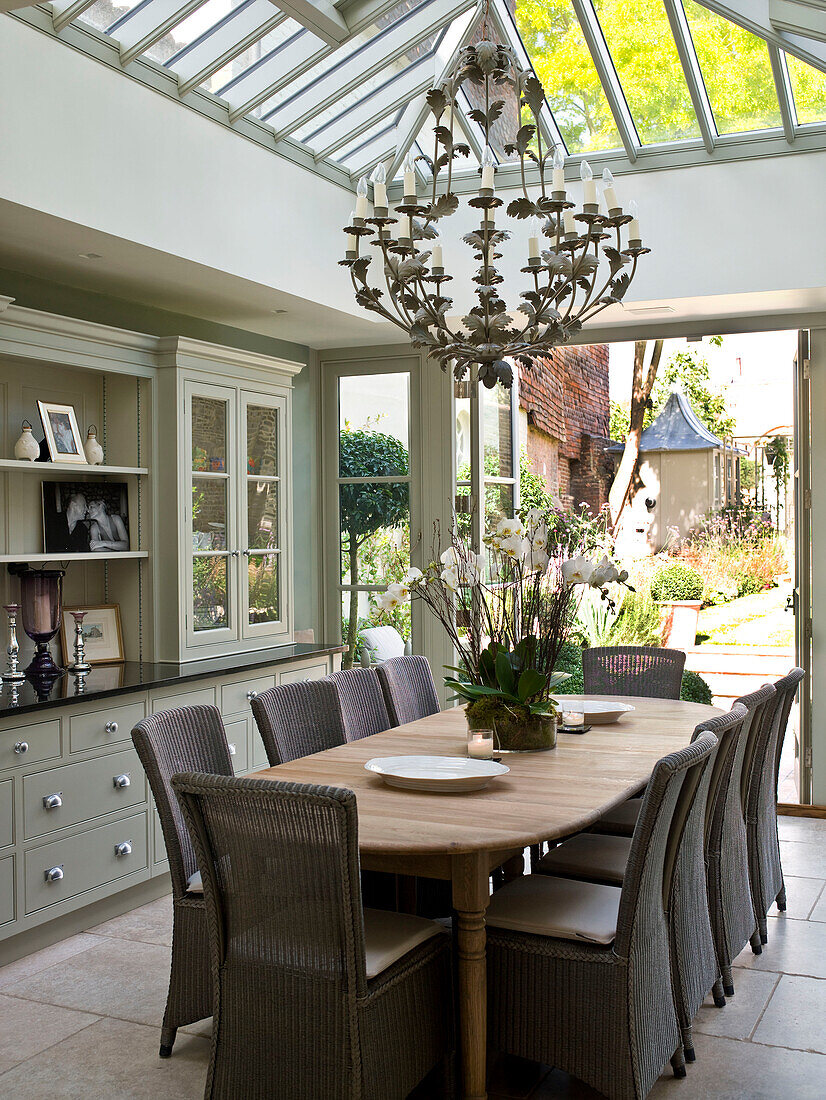 Ornate chandelier hangs above wooden dining table with with view to garden in West London townhouse conservatory extension England UK