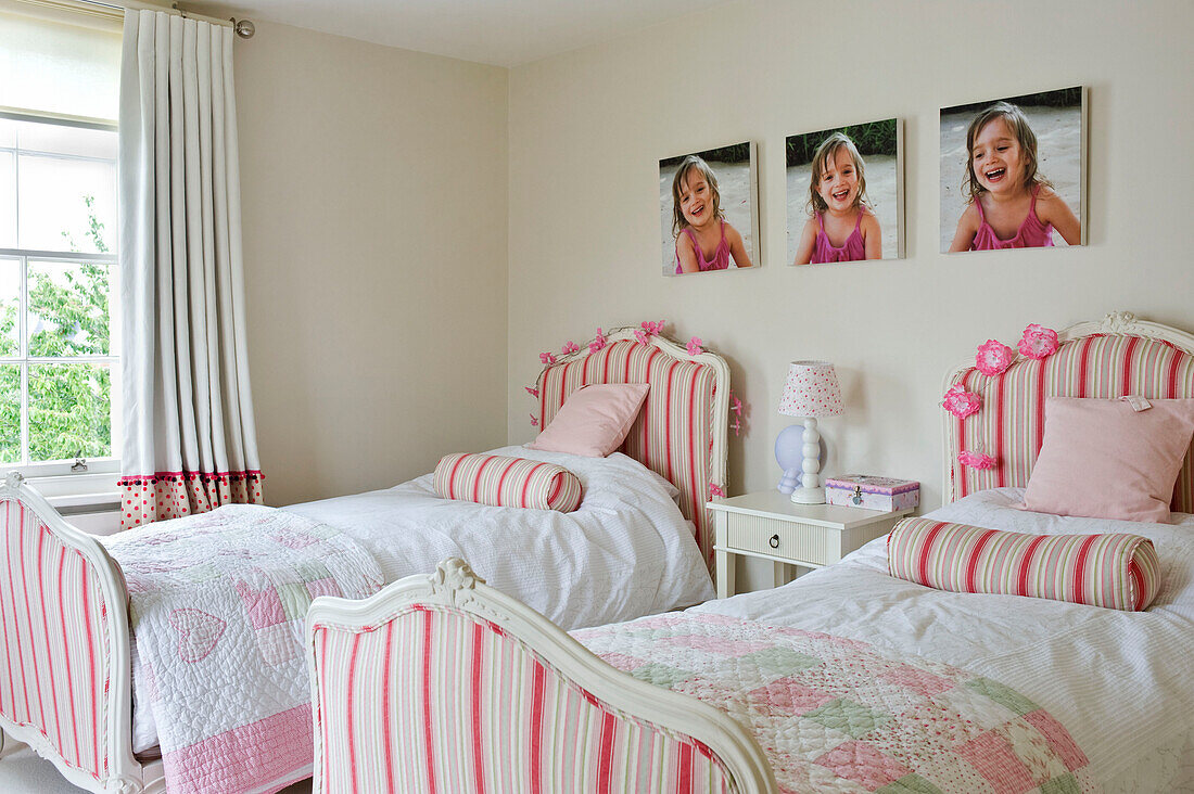 Pictures of young girl above twin beds upholstered in pink striped fabric in bedroom of West London townhouse England UK