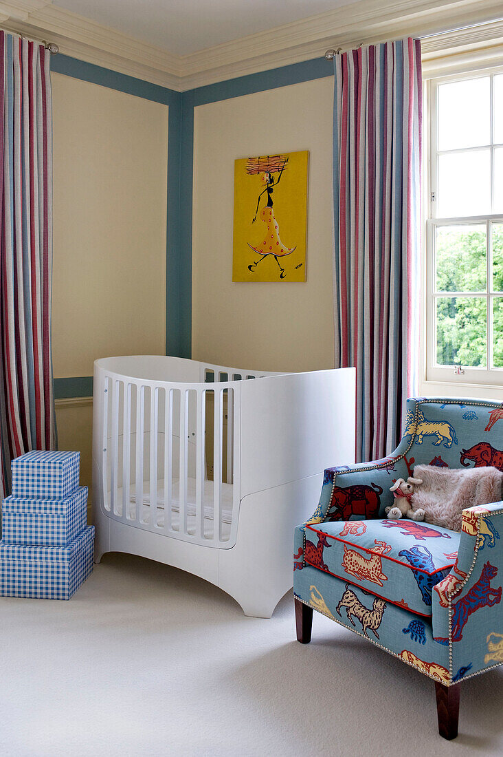 Checked storage boxes and crib with upholstered armchair in corner of children's room in West London townhouse England UK