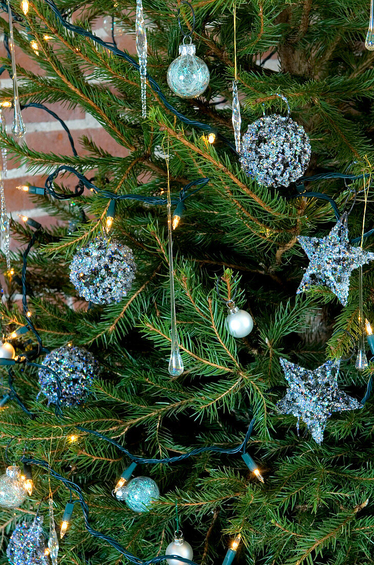 Metallische hellblaue Kugeln und Lichterketten am Weihnachtsbaum in einem Haus im ländlichen Suffolk, England UK