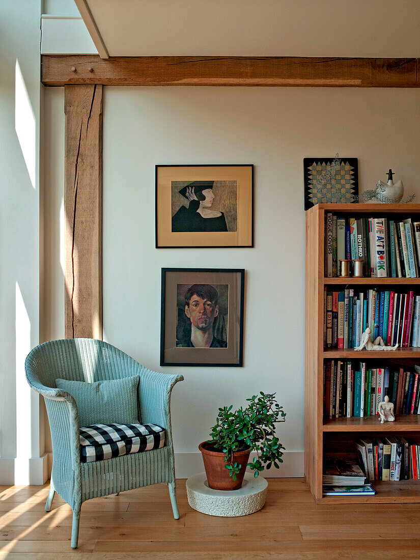 Kunstwerk und Bücherregal mit bemaltem Stuhl im Fachwerk-Wohnzimmer eines Familienhauses in Suffolk, England, UK