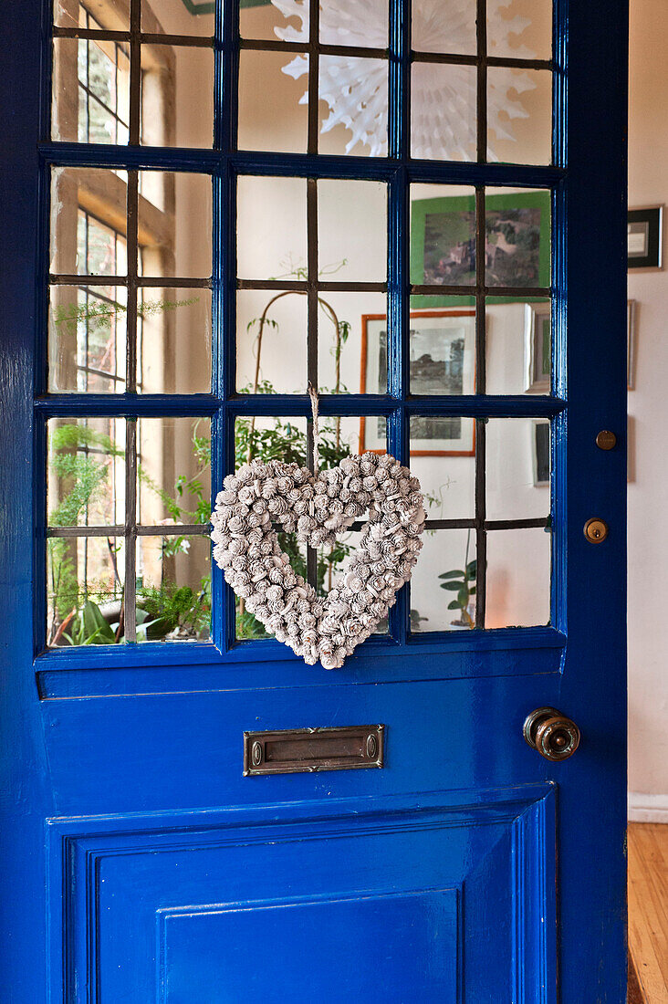 Herzförmiger Blumenkranz an der blauen Eingangstür eines Hauses in Forest Row, Sussex, England, Vereinigtes Königreich