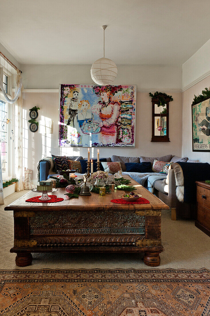 Weihnachtsdekoration im Wohnzimmer mit moderner Kunstleinwand und geschnitztem niedrigen Tisch in einem Haus in Forest Row, Sussex, England, UK