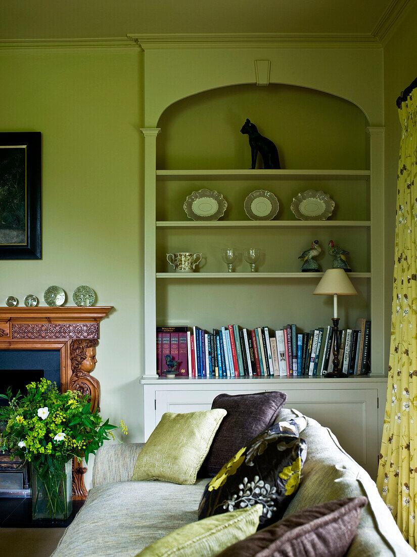 Eingelassene Bücherregale im Wohnzimmer mit Kissen auf dem Sofa in einem Haus im ländlichen Suffolk, England, UK