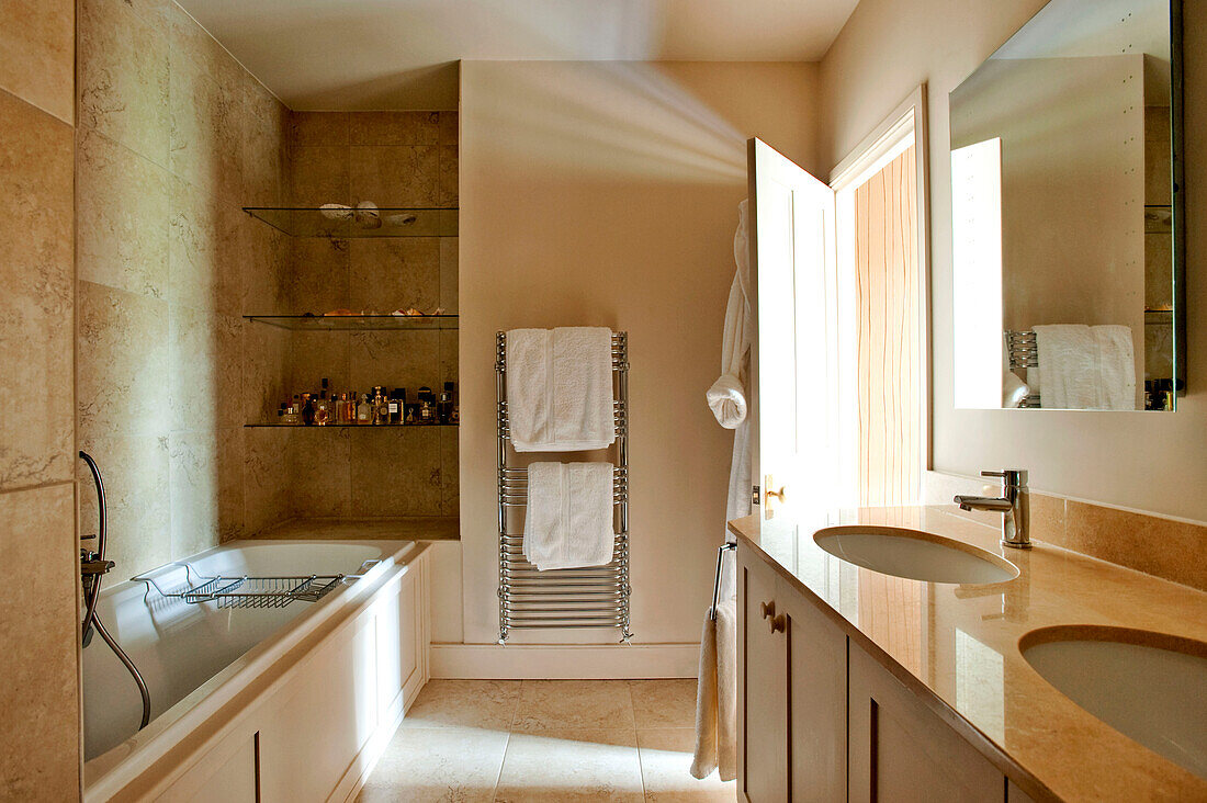 Sonnendurchflutetes Badezimmer mit Doppelwaschbecken und eingelassenen Glasregalen in einem Haus im ländlichen Suffolk England UK