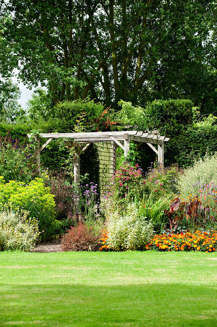 Sonnendurchflutete Pergola und Garten mit Rasen auf dem Gelände eines Landhauses in Suffolk England UK