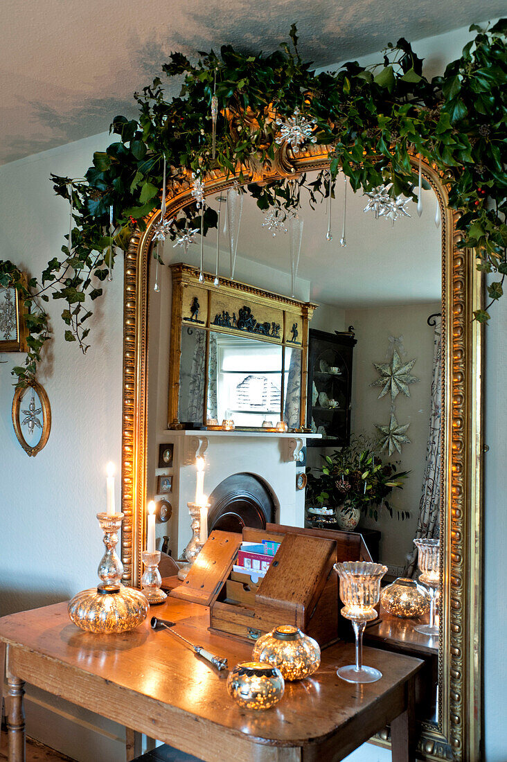 Silberne Kerzenständer auf Holztisch mit vergoldetem Spiegel und Blumengirlande in einem Haus in Walberton, West Sussex, England, UK