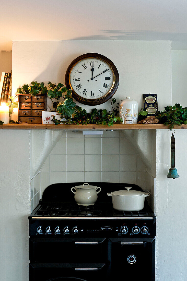 Töpfe auf einem Kochfeld unter einer Uhr und einem Regal mit Weihnachtsgirlande in einem Haus in Walberton, West Sussex, England, UK