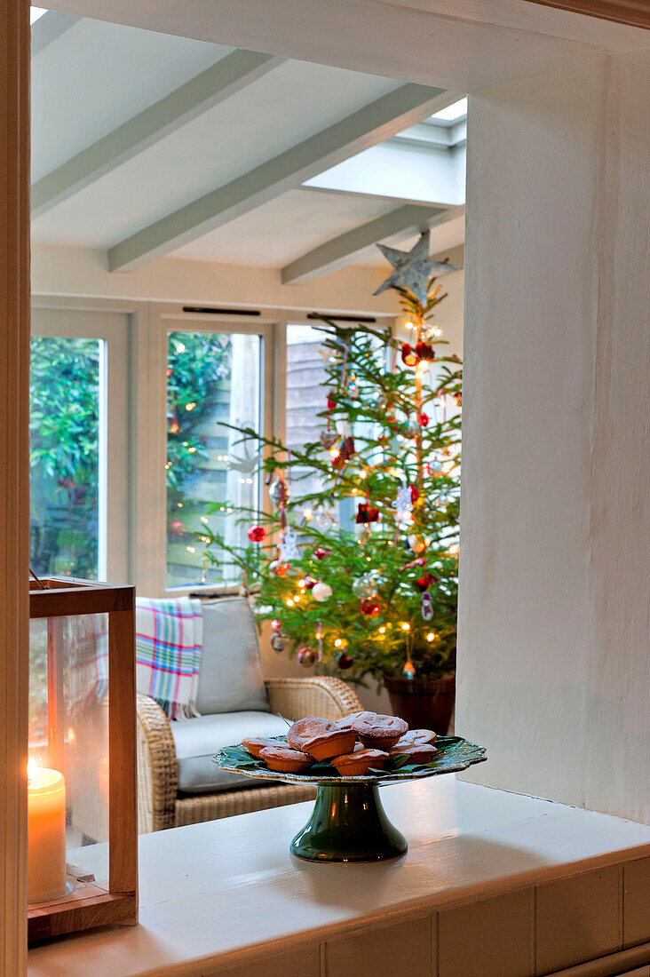 Torten mit Laternenkerzen und Blick auf den Wintergartenanbau mit Weihnachtsbaum in einem Haus in Walberton, West Sussex, England, Vereinigtes Königreich