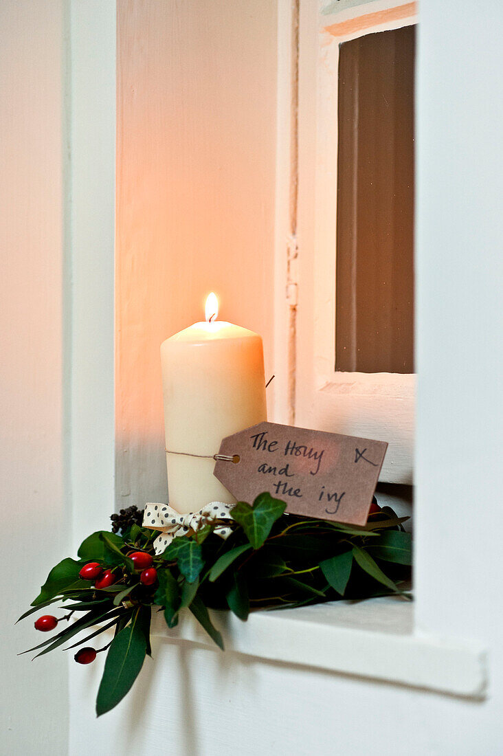 Beleuchtete Kerze mit Stechpalme und Efeu in einem Haus in Walberton, West Sussex, England, UK