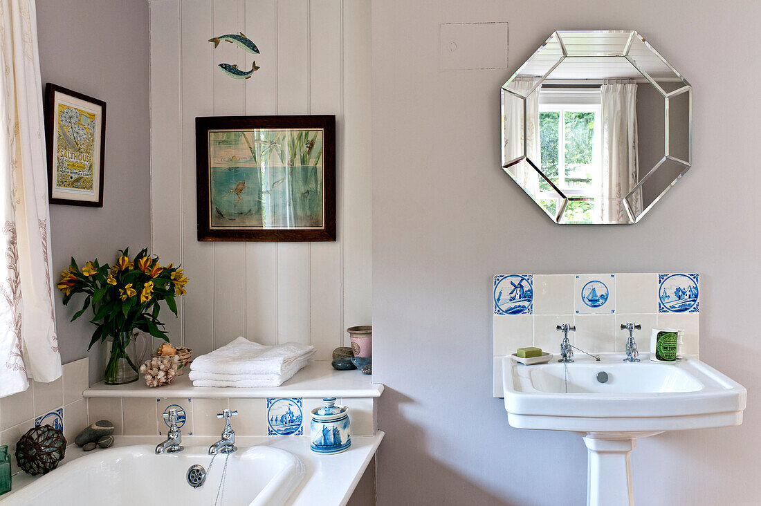 Schnittblumen und Ornamente mit achteckigem Spiegel über dem Sockelbecken im Badezimmer eines Hauses in Essex, England, Vereinigtes Königreich