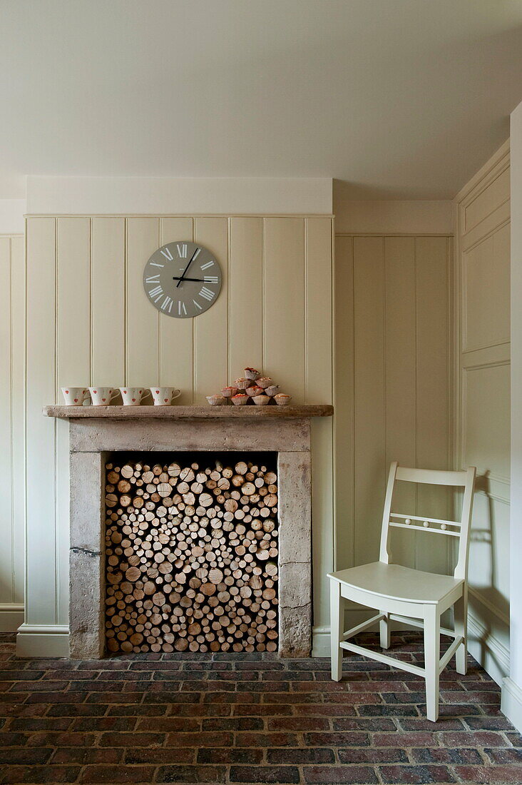 Chair beside fireplace full of logs in Buckinghamshire home, England, UK