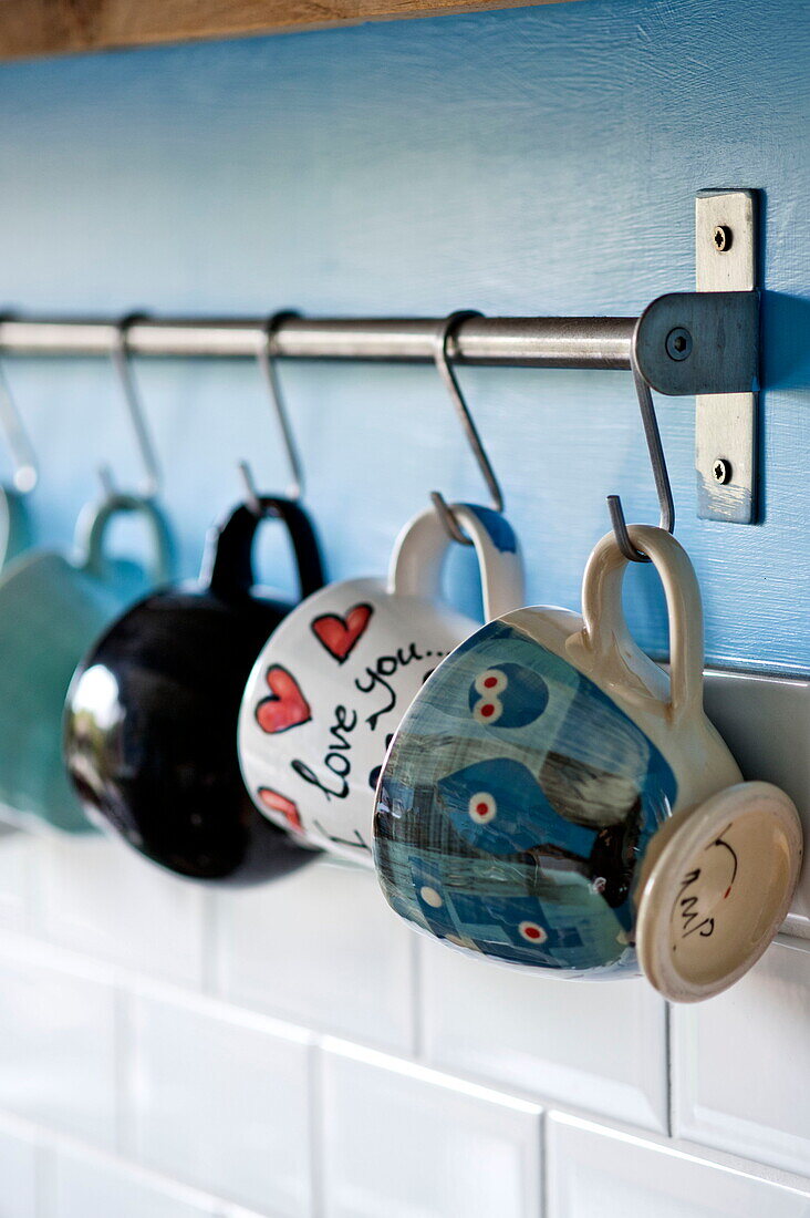 Porzellantassen hängen an Metallhaken in der Küche des Hauses der Familie Bovey Tracey, Devon, England, UK