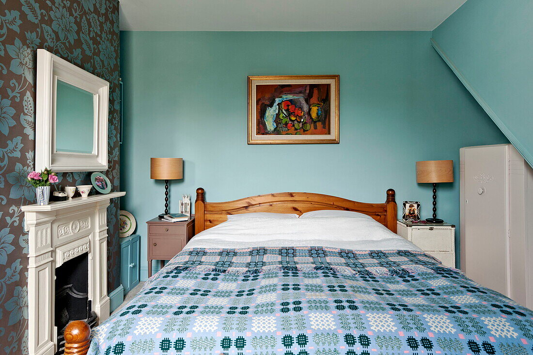 Kunstwerk über dem Bett mit blauem und weißem Bezug im Haus einer Familie in Bovey Tracey, Devon, England, UK
