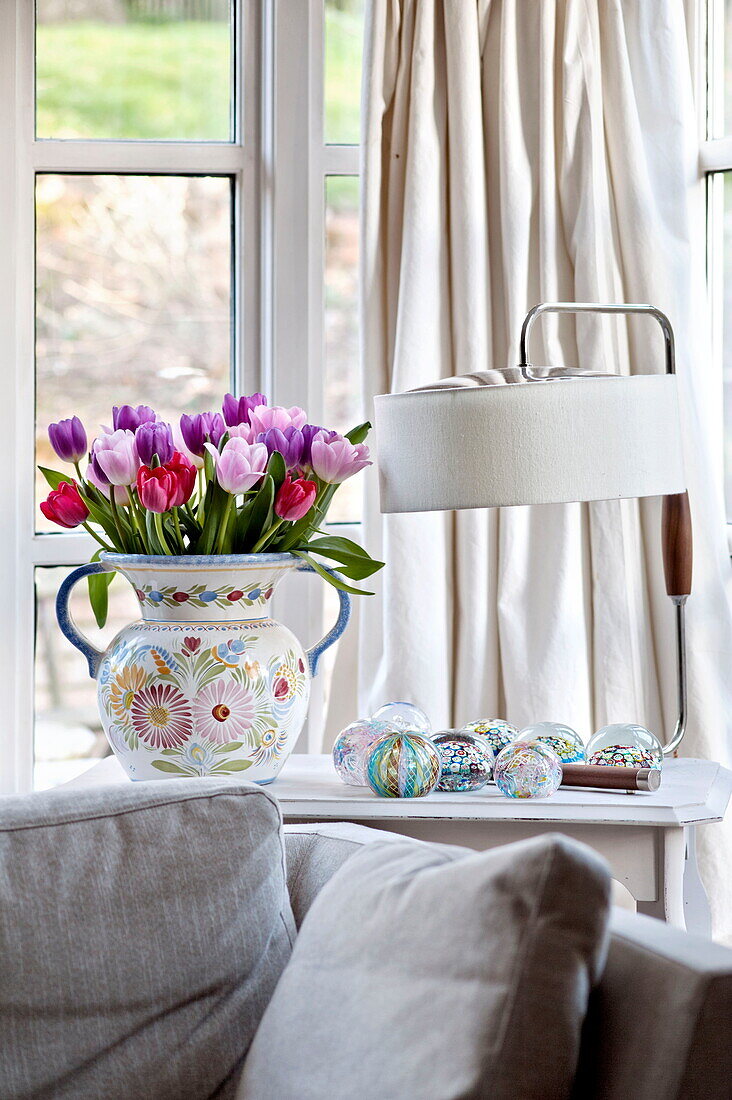 Cut tulips and lamp with cream curtains and sofa in living room of Suffolk farmhouse, England, UK