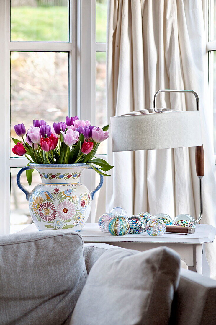 Geschnittene Tulpen und Lampe mit cremefarbenen Vorhängen und Sofa im Wohnzimmer eines Bauernhauses in Suffolk, England, UK