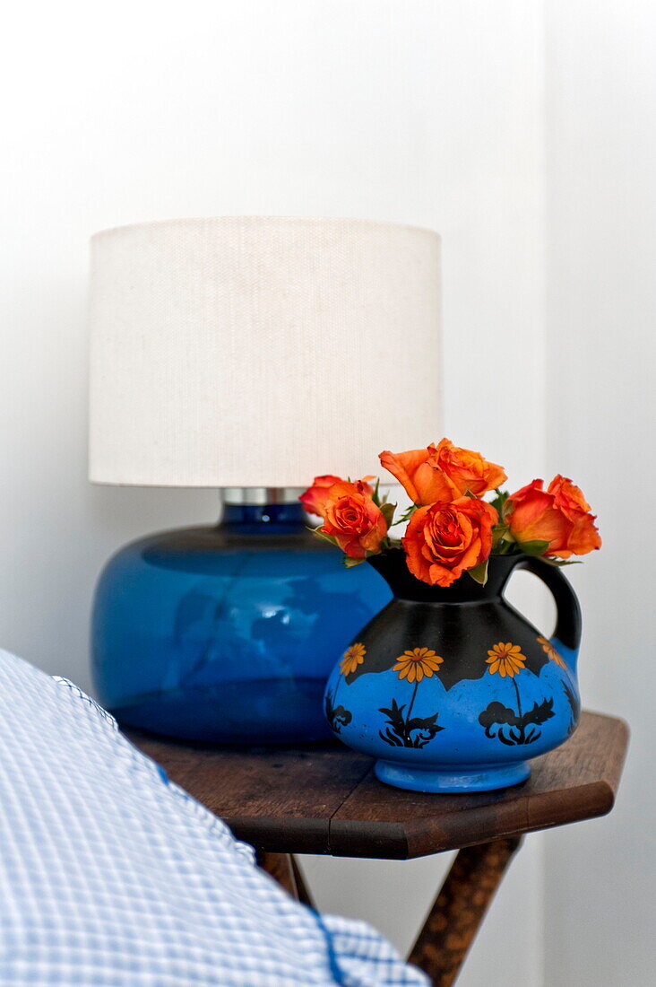 Cut roses in blue jug with lamp at bedside in Suffolk farmhouse, England, UK
