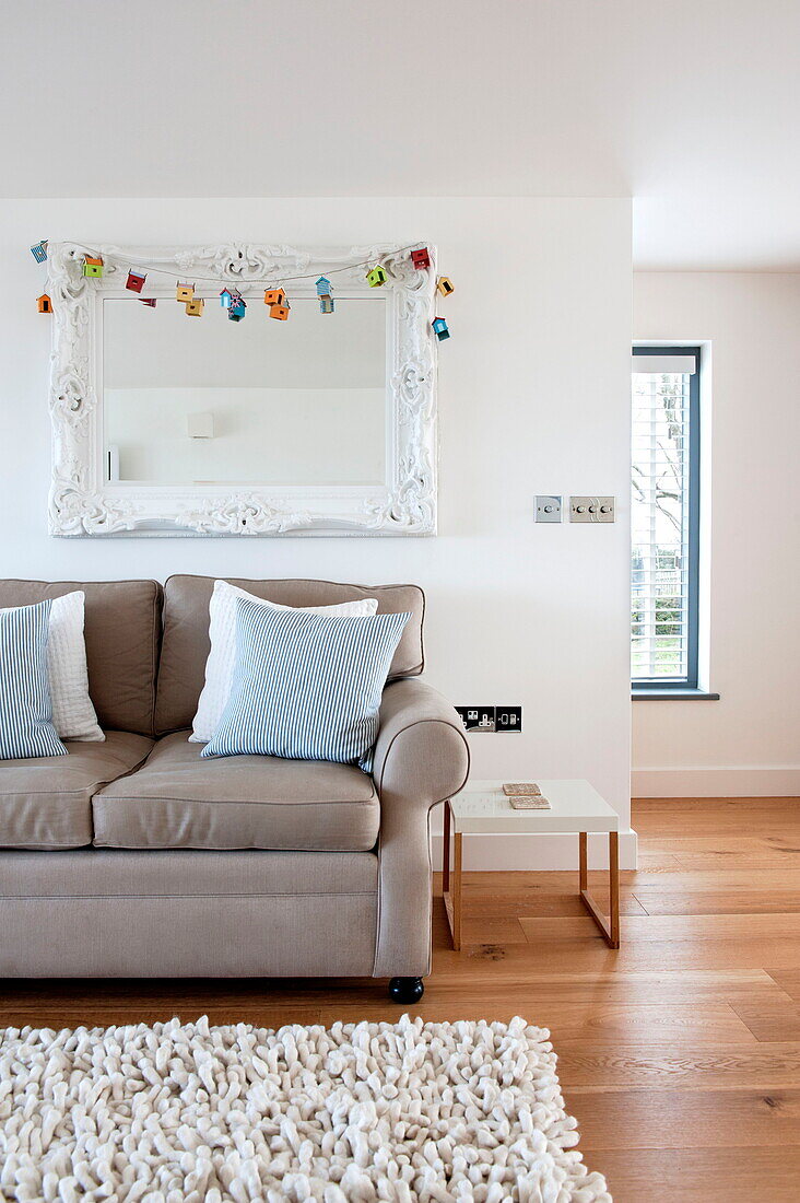 Two seater sofa below ornate white mirror in living room of Wadebridge home, Cornwall, England, UK