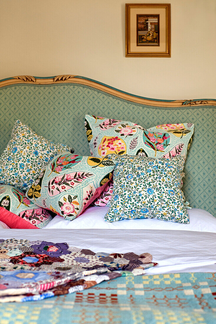 Blumen- und blattgemusterte Kissen auf dem Bett mit Patchwork-Decke in einem Haus in Hertfordshire, England, Vereinigtes Königreich