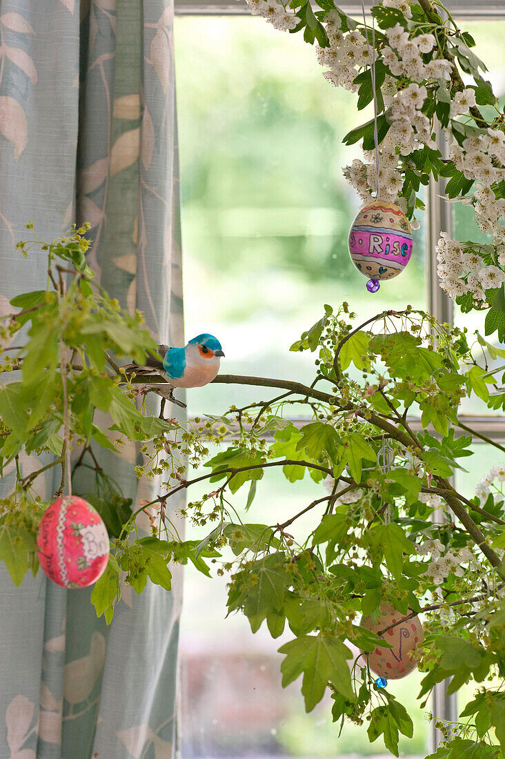 Artificial bird with hand-painted Easter eggs in spring blossom, Essex home, England, UK